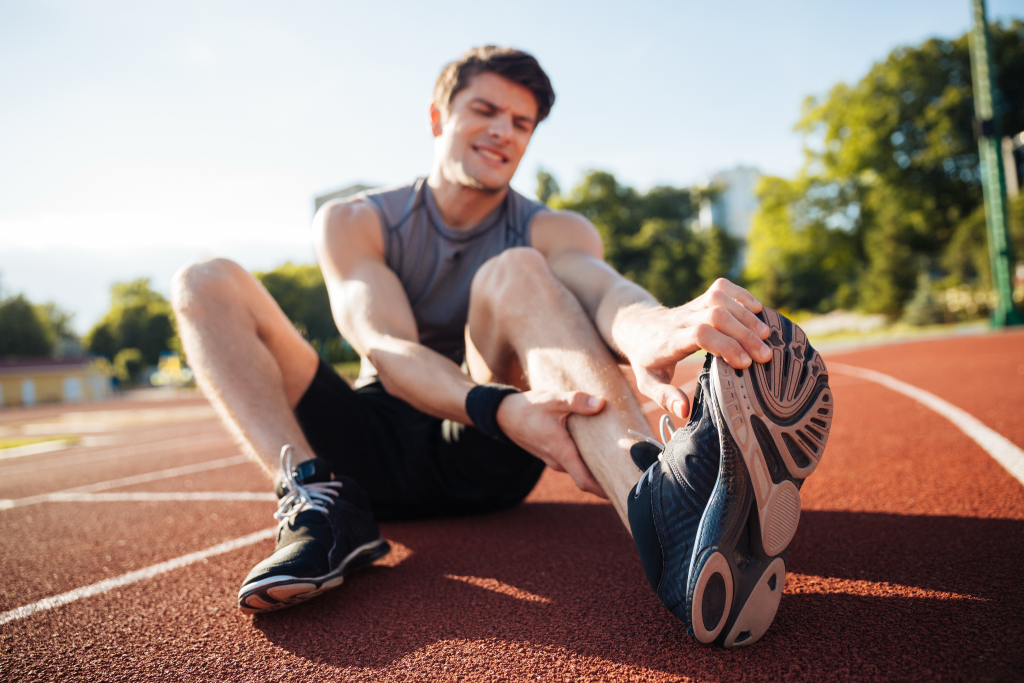 A young man in athletic wear sitting on a red running track, stretching and reaching toward his foot