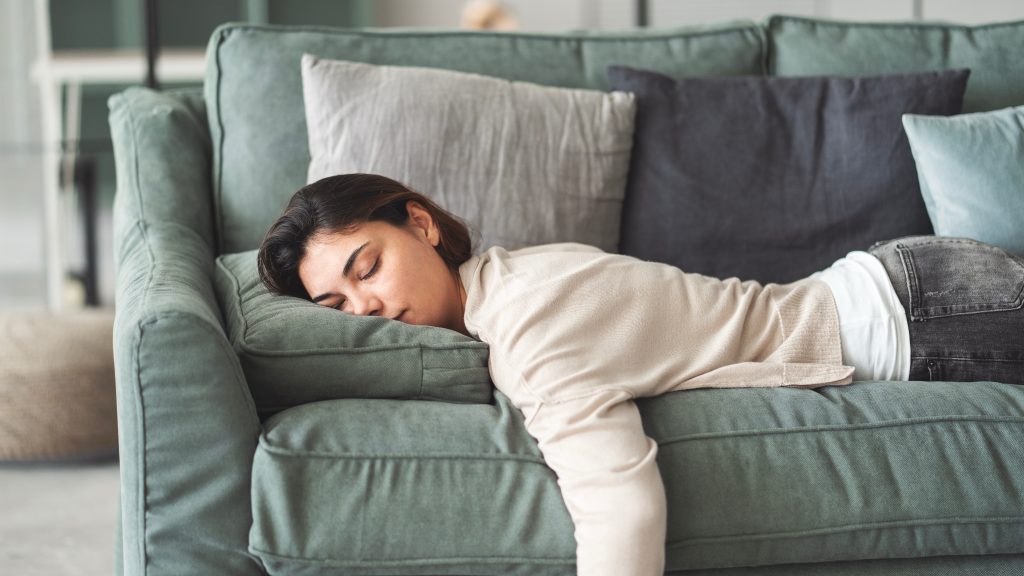 A young woman with dark hair sleeping on a teal couch cushion, eyes closed and head resting on her arm