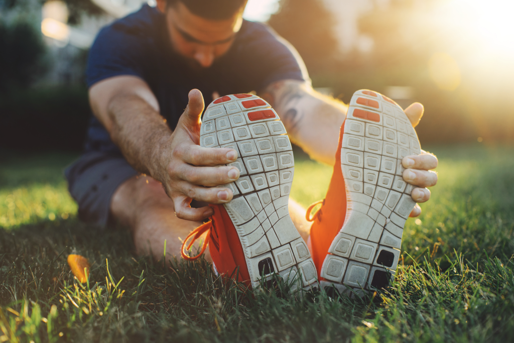 A person wearing orange and white athletic shoes while seated on grass and stretching