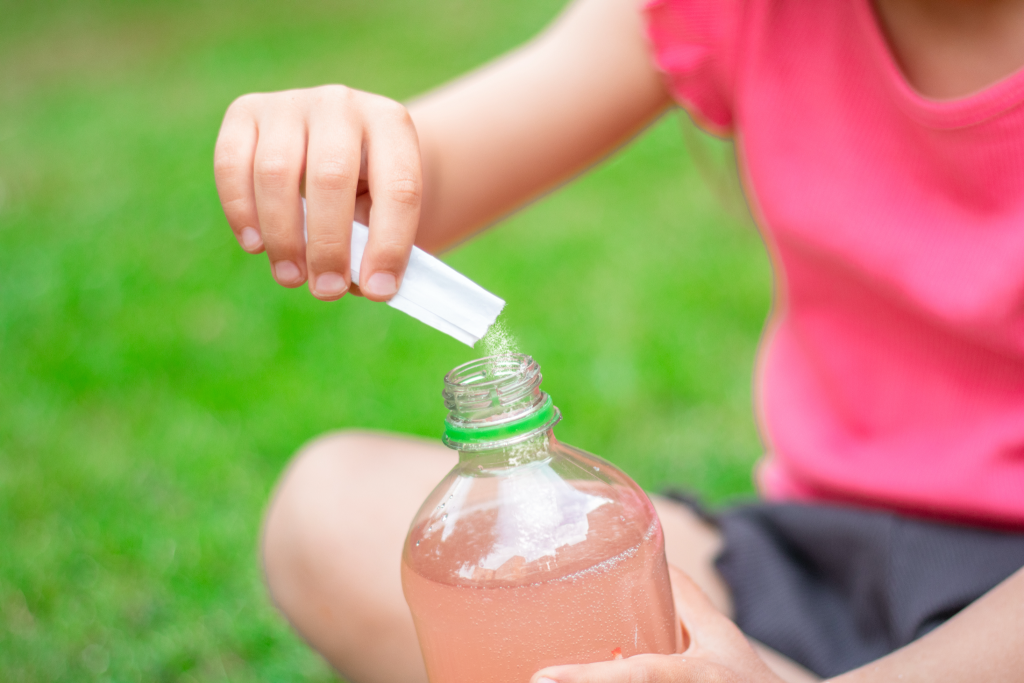 Female athlete pouring wearing pink electrolyte powder into a water bottle